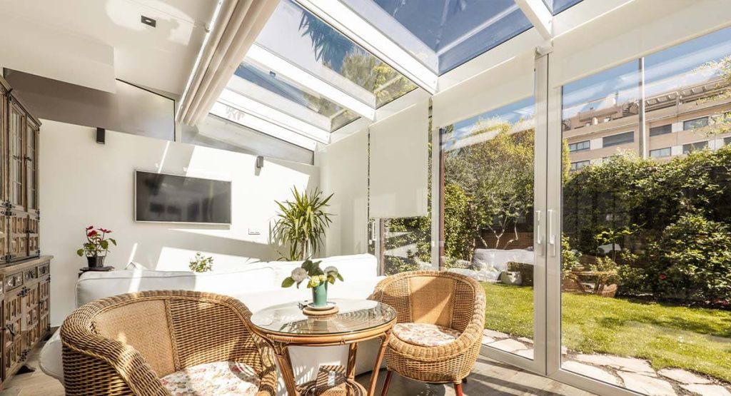 Installation de véranda aluminium avec toit vitré et baies coulissantes ouvrant sur un jardin urbain