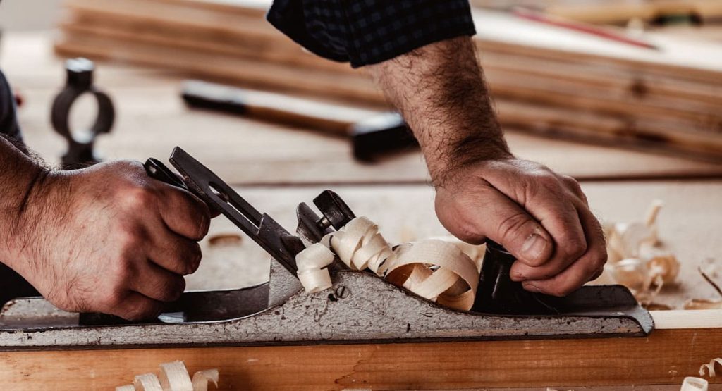 Utilisation d’un rabot manuel dans un atelier de menuiserie pour des finitions sur bois massif