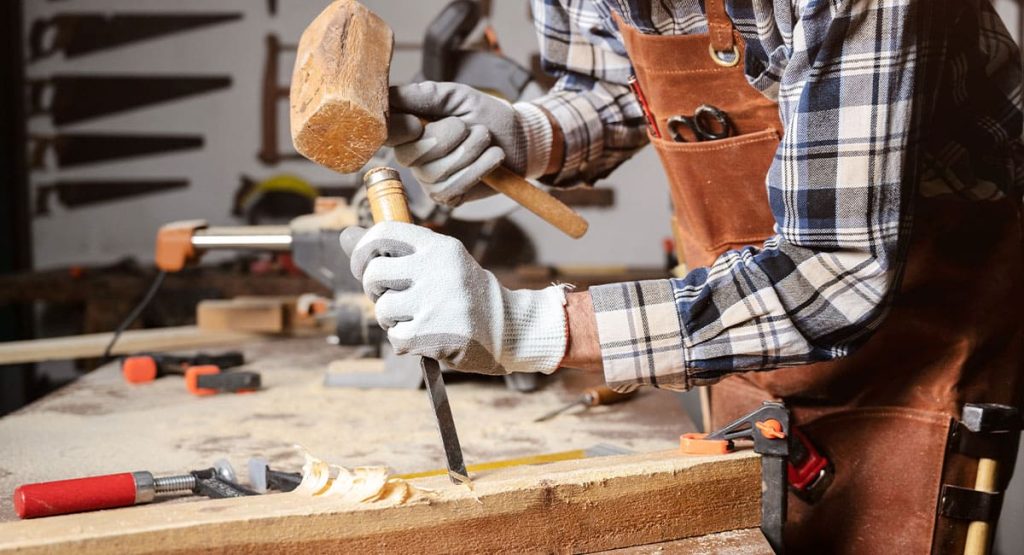Artisan menuisier utilisant un ciseau à bois et un maillet pour façonner une pièce en atelier