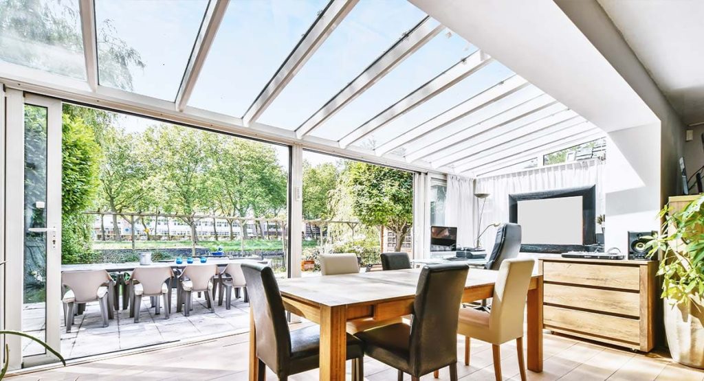Véranda avec toit vitré et baie coulissante donnant sur une terrasse arborée