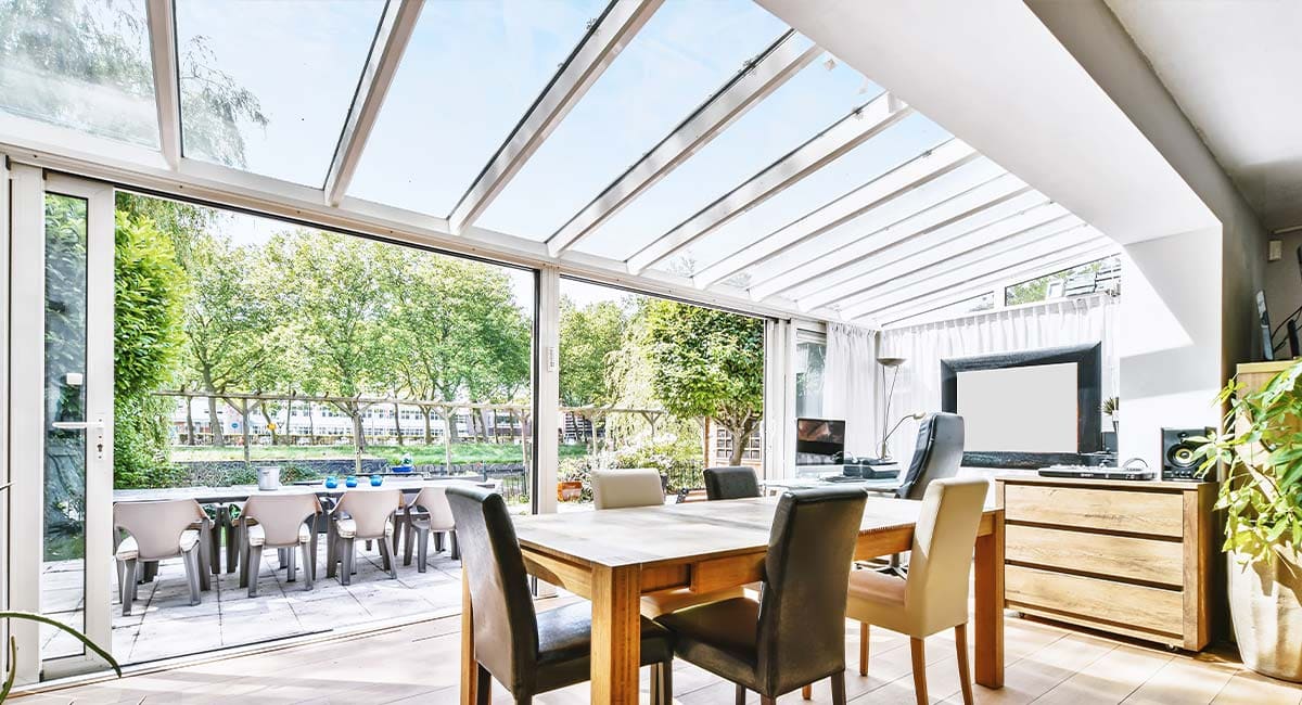 Véranda avec toit vitré et baie coulissante donnant sur une terrasse arborée